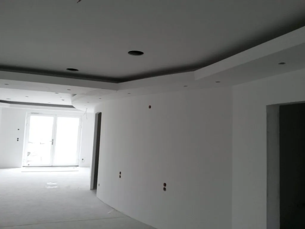 Offener Wohnraum mit umlaufender abgehängter Decke und Einbauspots.